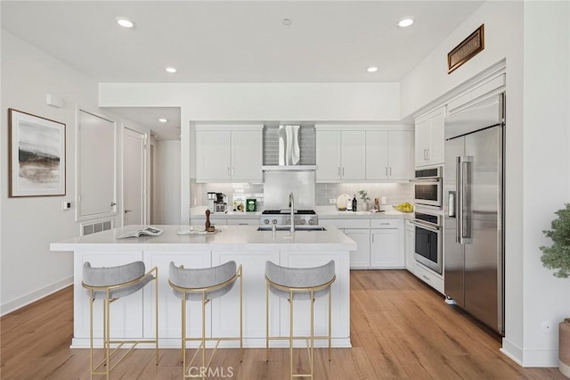 kitchen with built in fridge, light countertops, visible vents, backsplash, and a sink