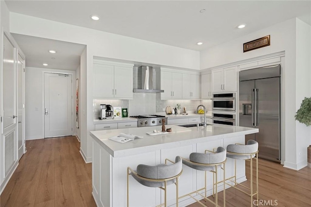 kitchen with appliances with stainless steel finishes, a sink, light countertops, wall chimney range hood, and backsplash