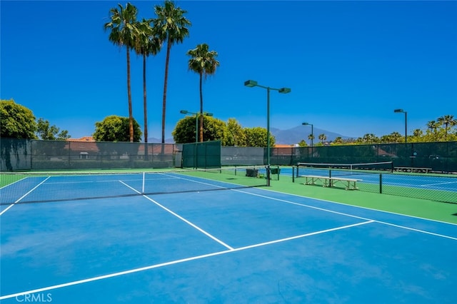 view of tennis court featuring community basketball court, fence, and a mountain view