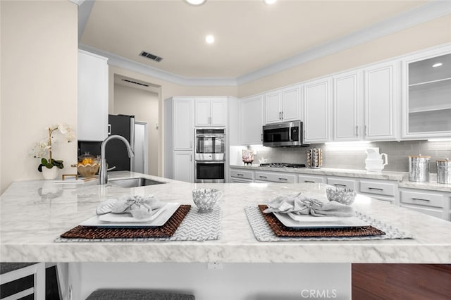 kitchen with light stone counters, stainless steel appliances, visible vents, backsplash, and a sink