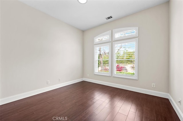 empty room with baseboards, visible vents, and dark wood-type flooring