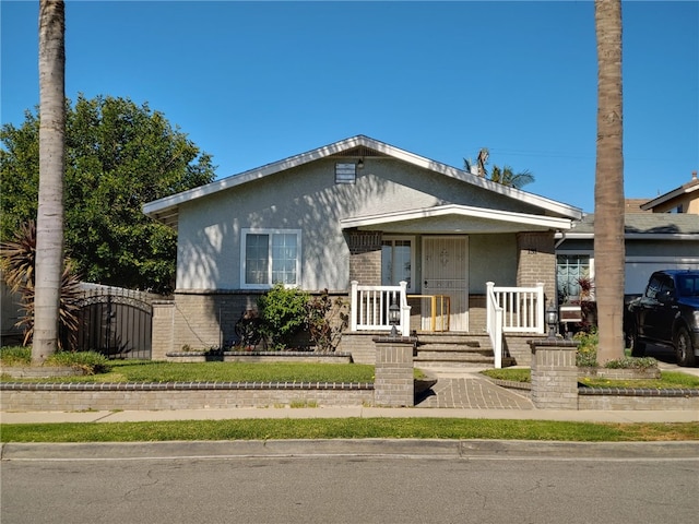 bungalow-style house featuring stucco siding, brick siding, covered porch, and a gate