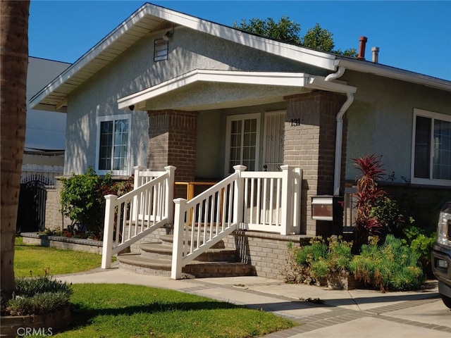 view of front of house featuring stucco siding, brick siding, and covered porch