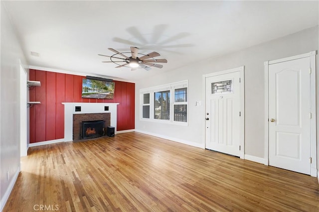 unfurnished living room featuring ceiling fan, a brick fireplace, wood finished floors, and baseboards