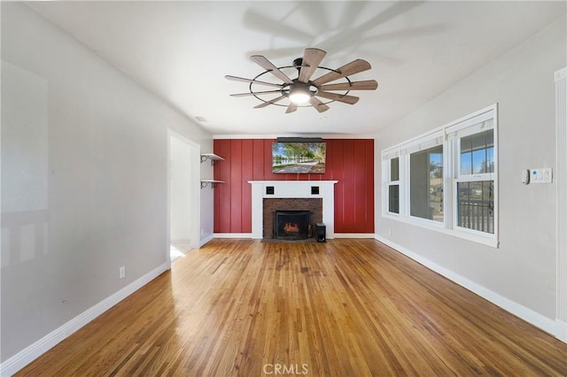 unfurnished living room with a brick fireplace, ceiling fan, baseboards, and wood finished floors