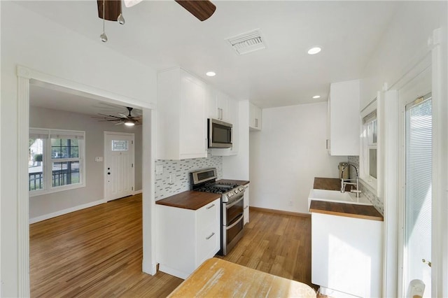 kitchen with tasteful backsplash, visible vents, white cabinets, appliances with stainless steel finishes, and light wood-style floors