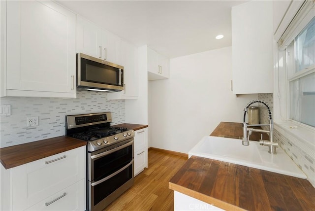 kitchen featuring a sink, light wood-style floors, wooden counters, appliances with stainless steel finishes, and tasteful backsplash