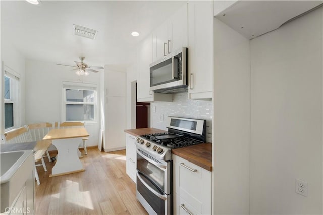 kitchen with butcher block counters, white cabinets, light wood-style floors, appliances with stainless steel finishes, and decorative backsplash