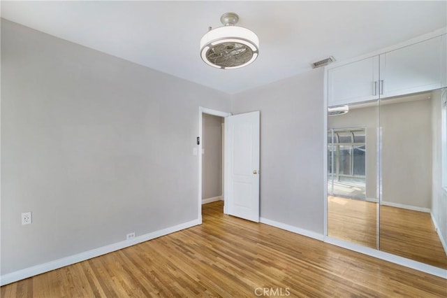 unfurnished bedroom featuring light wood-type flooring, baseboards, visible vents, and a closet