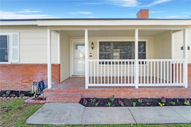 property entrance with covered porch, brick siding, and a chimney