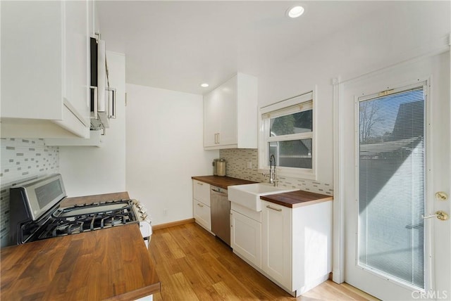 kitchen with light wood-style flooring, stainless steel appliances, butcher block counters, a sink, and decorative backsplash