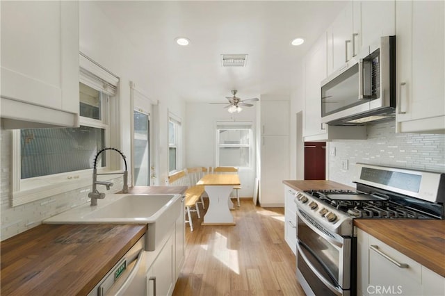 kitchen featuring light wood-type flooring, tasteful backsplash, butcher block countertops, and stainless steel appliances