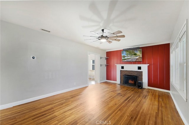 unfurnished living room with visible vents, a brick fireplace, ceiling fan, wood finished floors, and baseboards