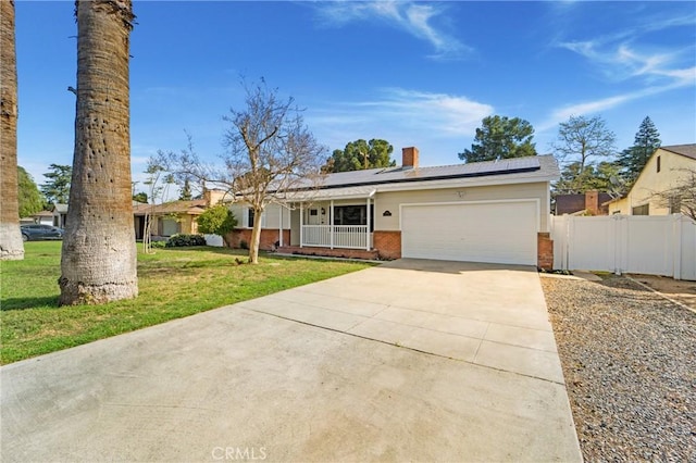 ranch-style house featuring solar panels, an attached garage, covered porch, fence, and a front lawn