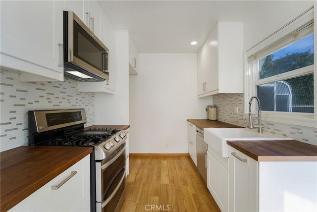 kitchen with stainless steel appliances, butcher block countertops, a sink, white cabinetry, and light wood finished floors