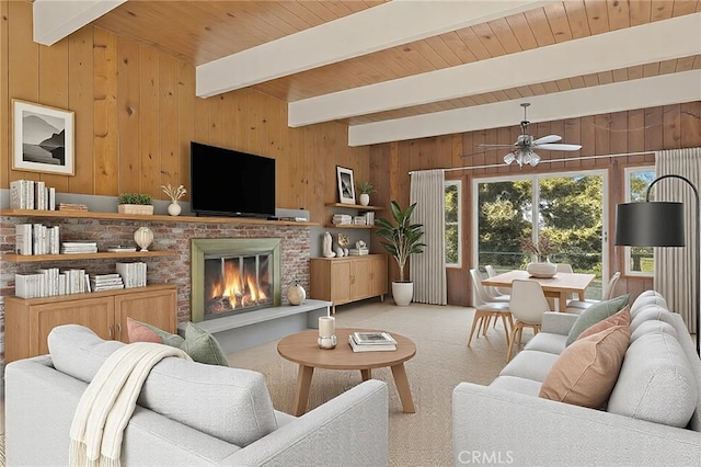 living room featuring ceiling fan, beamed ceiling, carpet floors, wood walls, and a fireplace