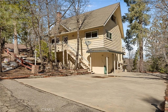 rustic home with a shingled roof, a patio area, a chimney, and stairs