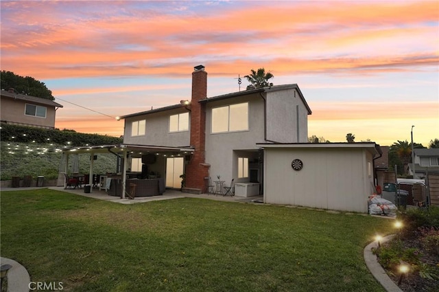 back of property featuring stucco siding, a chimney, a lawn, and a patio