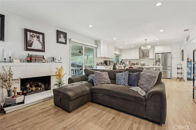 living room featuring a chandelier, light wood-type flooring, a fireplace, and recessed lighting