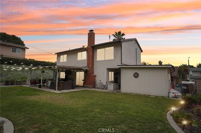 back of house at dusk with a yard, a patio, a chimney, and stucco siding