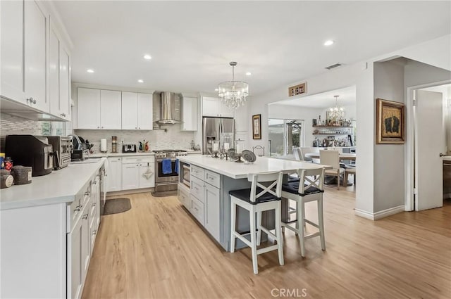 kitchen with stainless steel appliances, a breakfast bar, a notable chandelier, and wall chimney range hood