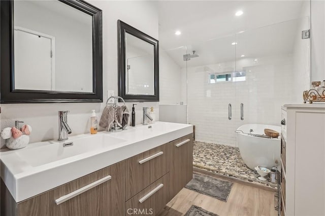 full bathroom with double vanity, a shower stall, a sink, and wood finished floors