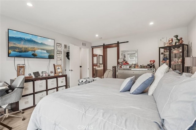 bedroom with a barn door, light wood-type flooring, visible vents, and recessed lighting