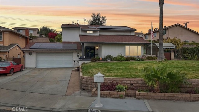 traditional-style house featuring a garage, solar panels, concrete driveway, and a yard