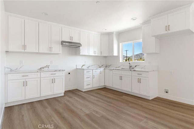 kitchen featuring a sink, under cabinet range hood, white cabinetry, light wood finished floors, and baseboards