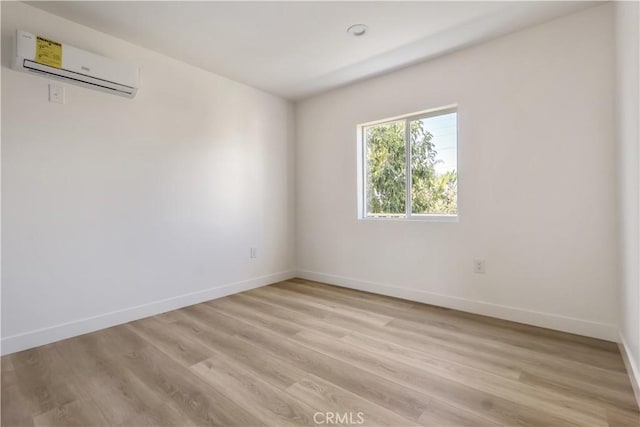 unfurnished room featuring baseboards, light wood finished floors, and a wall unit AC