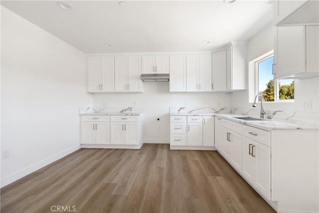 kitchen featuring a sink, under cabinet range hood, white cabinets, light wood finished floors, and baseboards