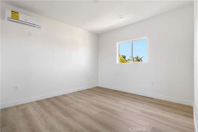 unfurnished room with baseboards, light wood-style floors, and an AC wall unit