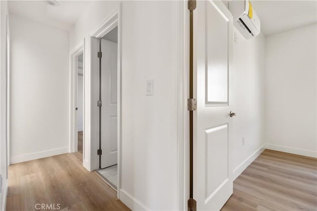 hall with a wall unit AC, baseboards, and light wood finished floors