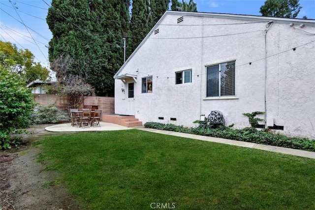 rear view of house with fence, stucco siding, crawl space, a patio area, and a lawn