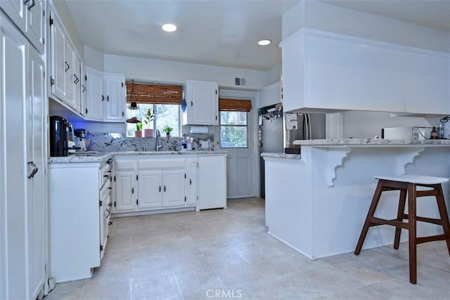 kitchen with a sink, visible vents, a breakfast bar, and white cabinets