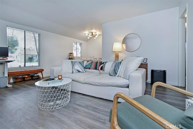 living room featuring an inviting chandelier, lofted ceiling, baseboards, and wood finished floors