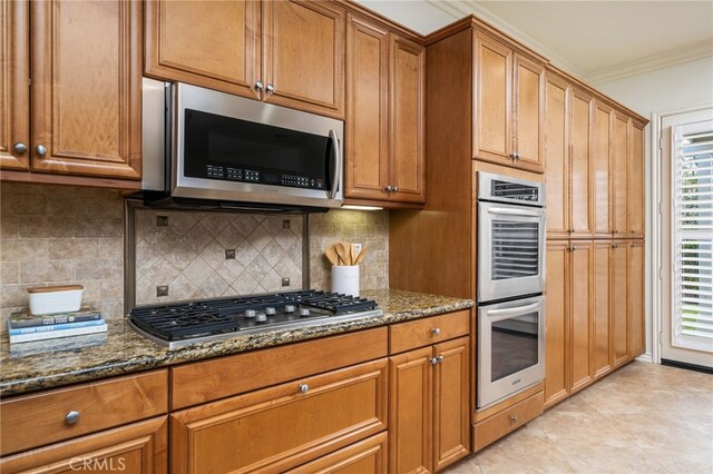 kitchen featuring tasteful backsplash, ornamental molding, brown cabinets, dark stone countertops, and stainless steel appliances