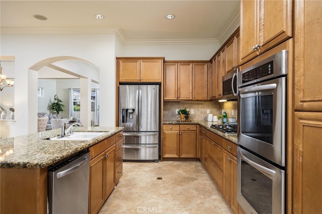 kitchen with stone countertops, a sink, appliances with stainless steel finishes, tasteful backsplash, and brown cabinetry