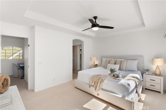 bedroom featuring light carpet, baseboards, arched walkways, ceiling fan, and a tray ceiling