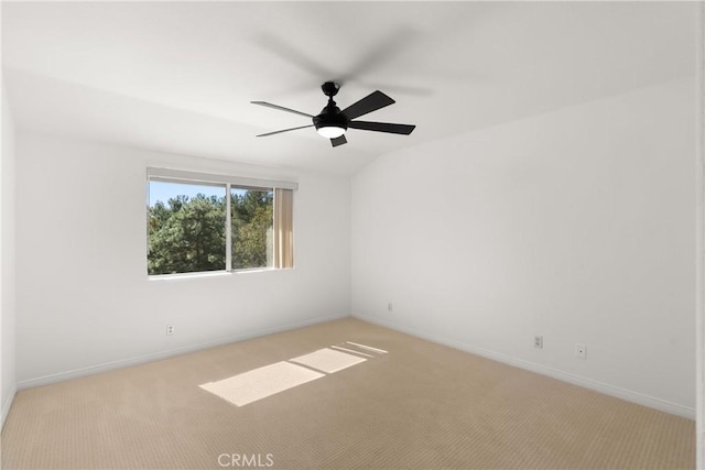 spare room with a ceiling fan, light carpet, vaulted ceiling, and baseboards