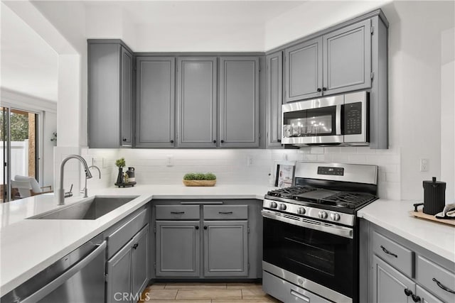 kitchen with stainless steel appliances, a sink, light countertops, and gray cabinetry