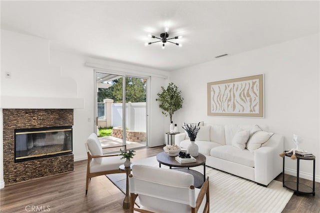 living area featuring a glass covered fireplace, visible vents, baseboards, and wood finished floors