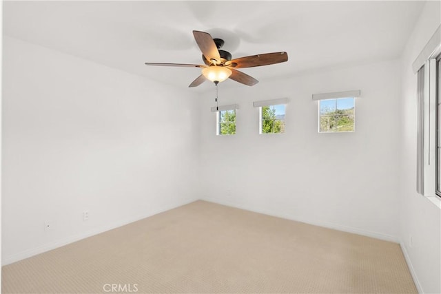 spare room with a healthy amount of sunlight, baseboards, a ceiling fan, and light colored carpet