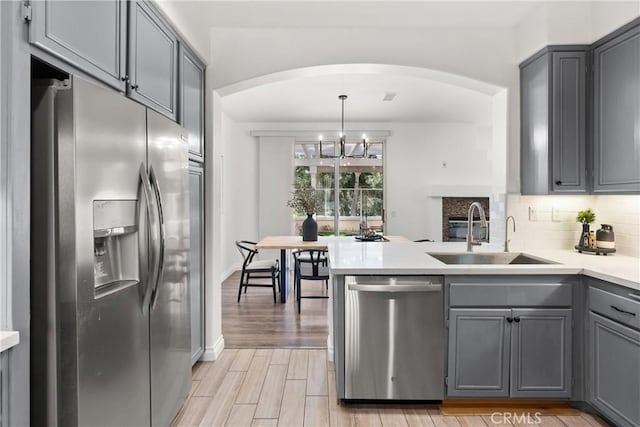 kitchen with gray cabinetry, stainless steel appliances, a peninsula, a sink, and tasteful backsplash