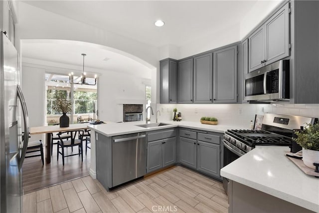 kitchen featuring decorative backsplash, wood tiled floor, gray cabinets, stainless steel appliances, and a sink