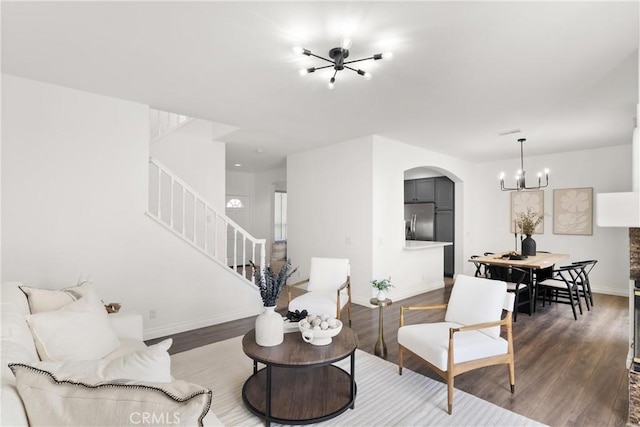 living area featuring arched walkways, wood finished floors, baseboards, and stairs