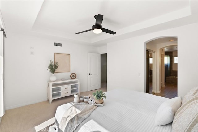 bedroom featuring visible vents, arched walkways, a ceiling fan, a tray ceiling, and carpet floors