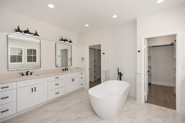 bathroom with a sink, a freestanding bath, marble finish floor, double vanity, and a walk in closet