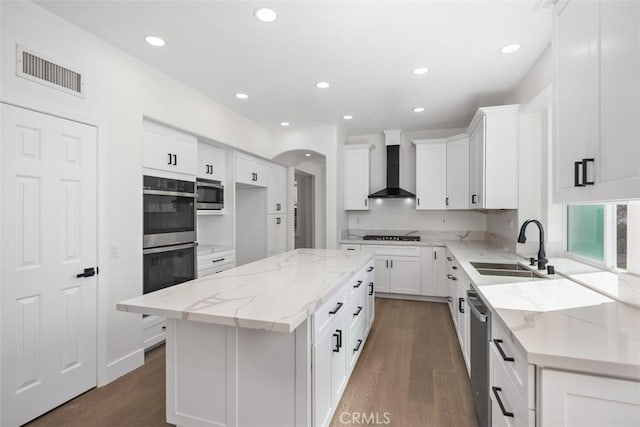 kitchen with visible vents, light stone counters, stainless steel appliances, wall chimney range hood, and a sink