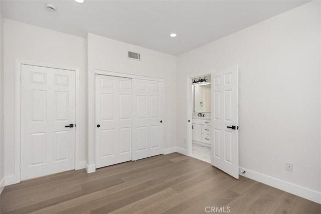 unfurnished bedroom with recessed lighting, wood finished floors, visible vents, baseboards, and ensuite bath